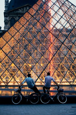 Due amici in bicicletta osservano la piramide del Louvre al tramonto